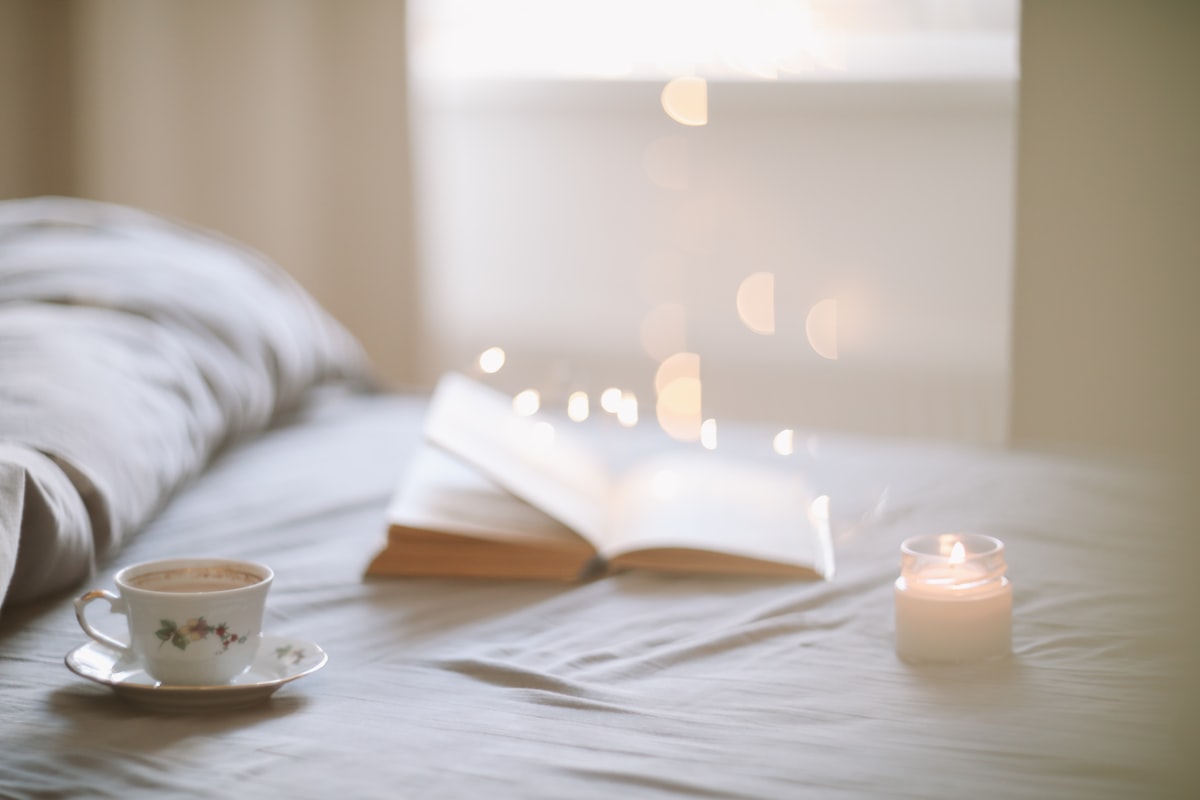 Cozy bedroom with warm morning light, coffee cup and open book on white linen