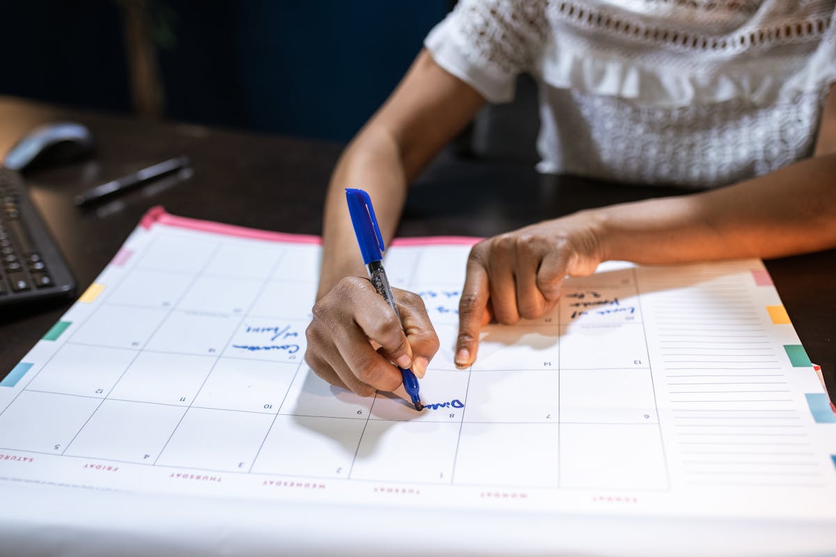 Woman writing on a paper desk calendar, planning and time management